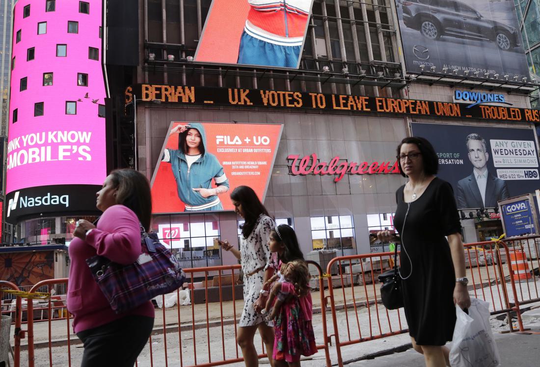 People walk past a news ticker that reads 